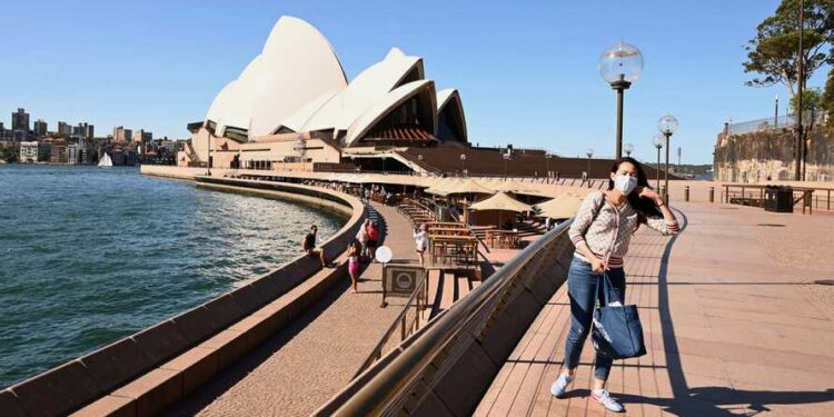 A lone tourist poses for a photo in Circular Quay in Sydney on March 20, 2020, after Australia moved to seal off its borders the day before, announcing unprecedented bans on entry for non-residents in the hope of stemming the rise of COVID-19 coronavirus infections. (Photo by PETER PARKS / AFP)