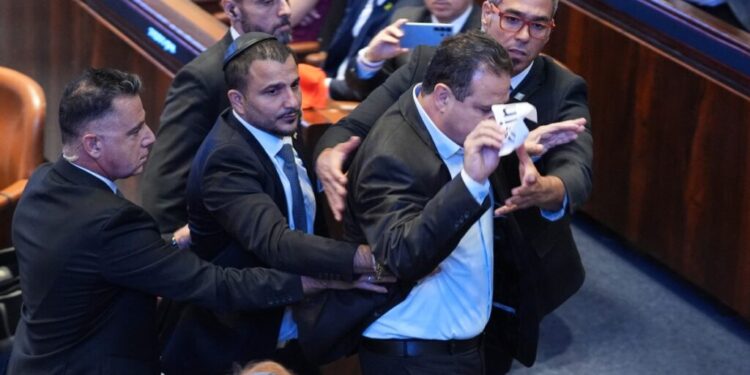 Israeli Knesset member Ayman Odeh (2R) is escorted out after holding a sign reading "Recognise Palestine" during a speech by US President Donald Trump at the Israeli parliament, the Knesset, in Jerusalem on October 13, 2025. Hamas handed over the 20 surviving Israeli hostages on October 13 under a ceasefire agreement, as the US president and other world leaders geared up for a summit on Gaza. The releases are part of a ceasefire agreement brokered by the US president, with Israel due in return to free nearly 2,000 detainees held in its jails in exchange. (Photo by Evan Vucci / POOL / AFP)
